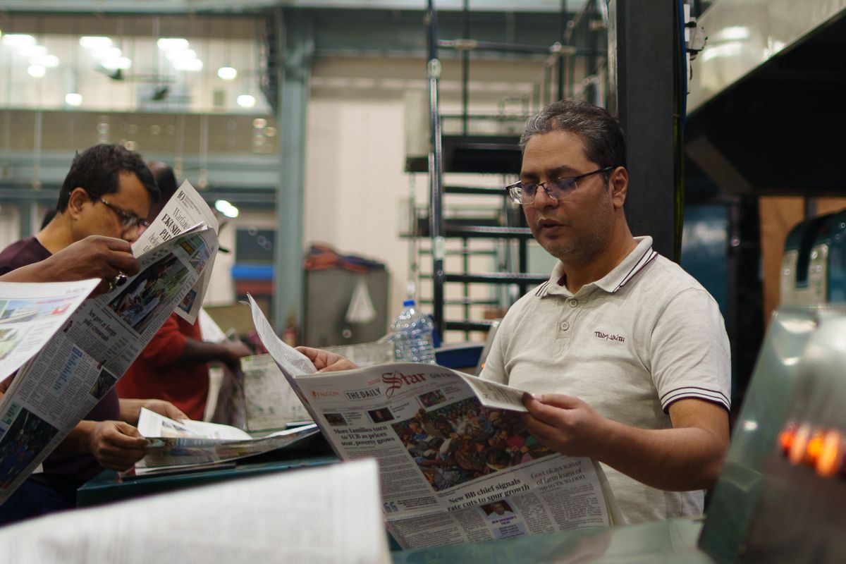 Workers reading freshly printed newspapers at a printing press